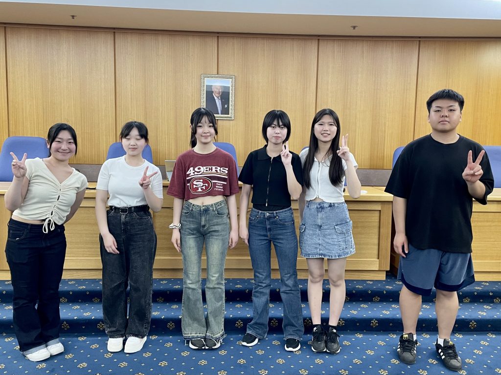Six Japanese students in the Bathurst council chambers in front of a photo of the King